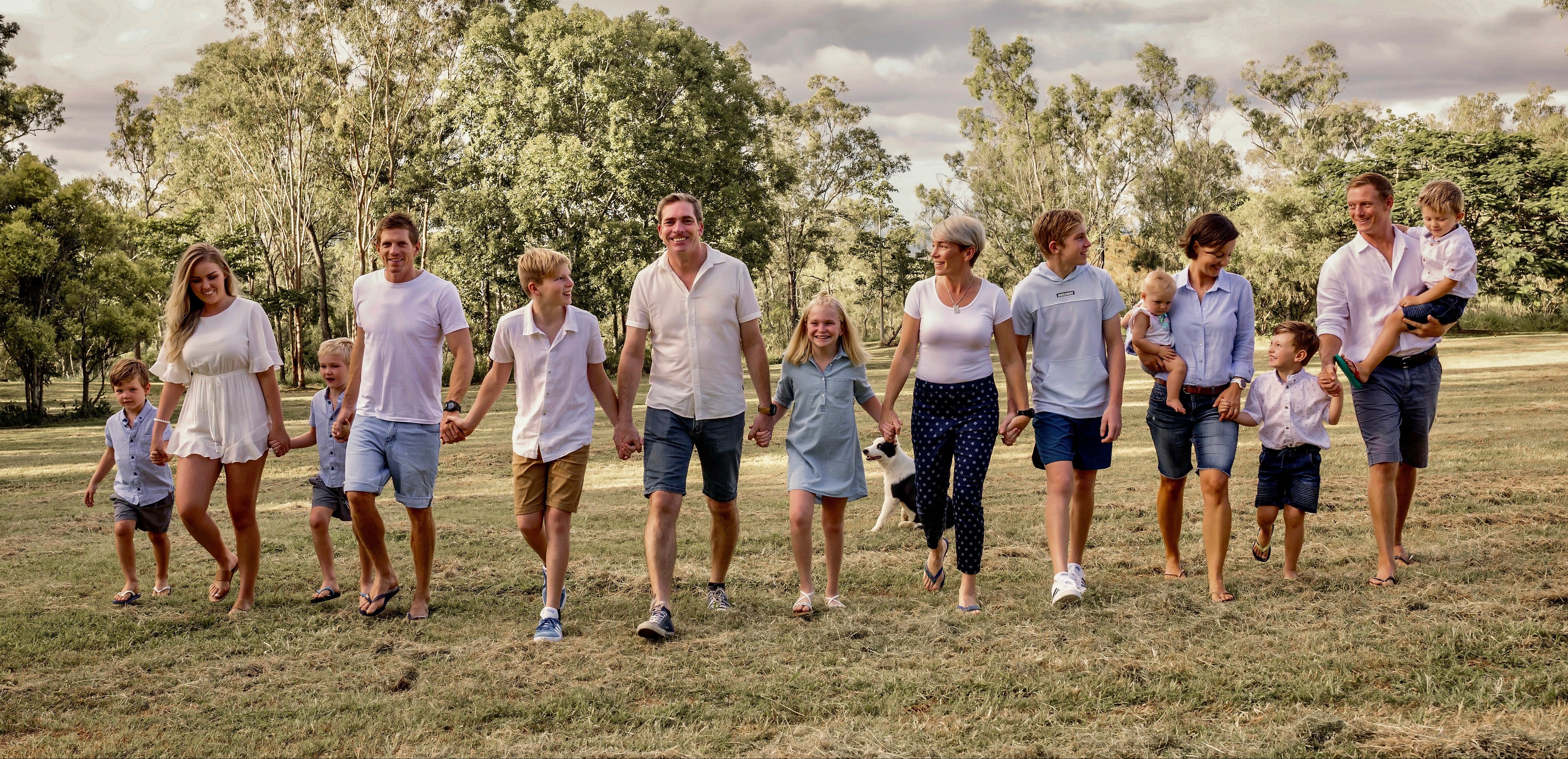 Family of 12 standing in a line on a grassy field with trees in the background. The family of Skybury farms.